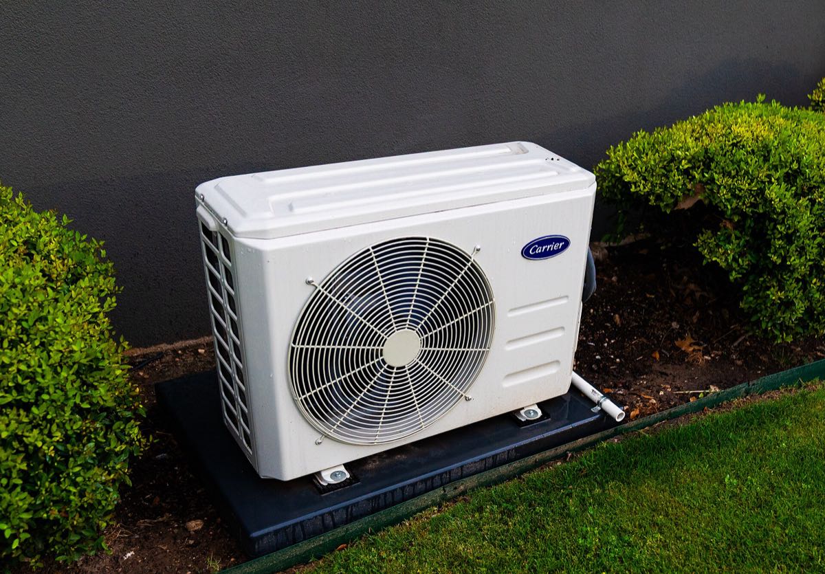 Condensadora de ar-condicionado nova, instalada sobre base, com jardim ao redor